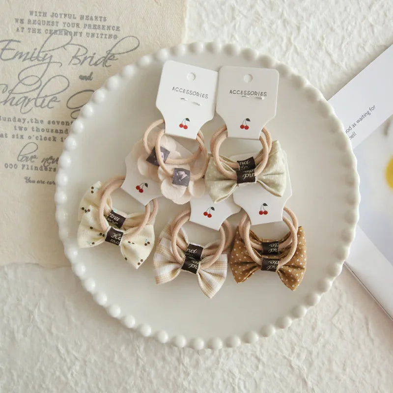 Six soft cotton hair ties for babies and girls, featuring bows in various neutral patterns and a flower design.