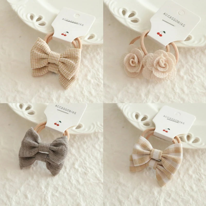 Set of four soft cotton hair ties for babies and girls: two plaid bows, one solid bow, and one with two fabric flowers.