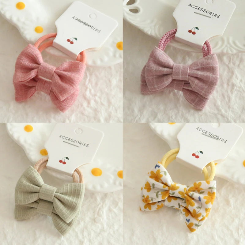 Four soft cotton hair ties for babies and girls, featuring delicate bows in pink, lavender, sage green, and a yellow floral print.