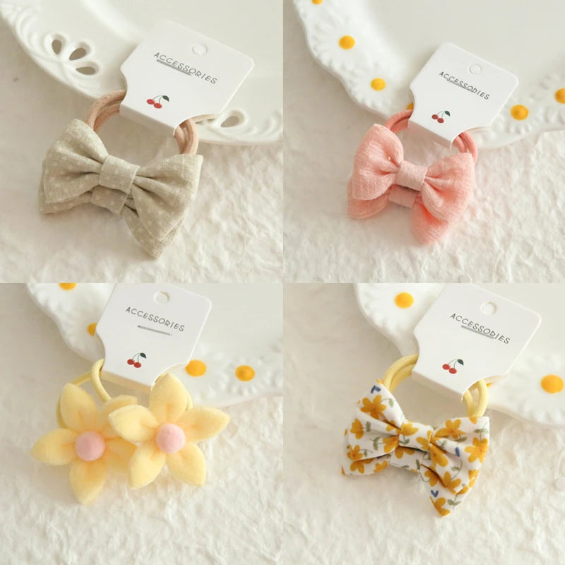 Four delicate cotton hair ties for babies and girls: two with bows (beige, pink) and two with floral designs (yellow flowers, yellow floral print bow).
