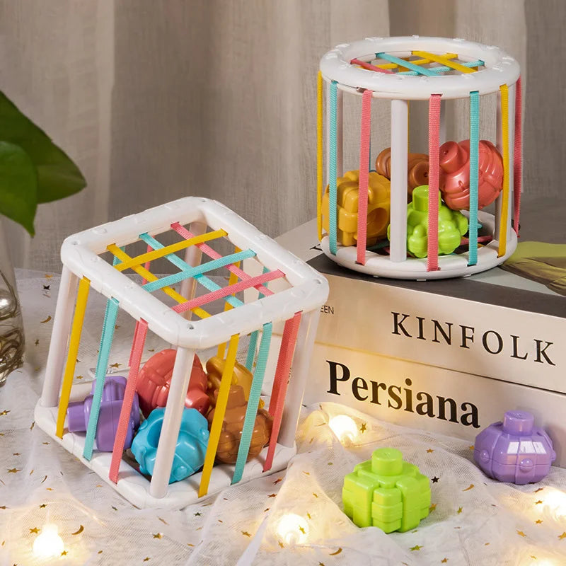 Montessori shape sorter cube and cylinder with colorful elastic bands and chunky plastic shapes.
