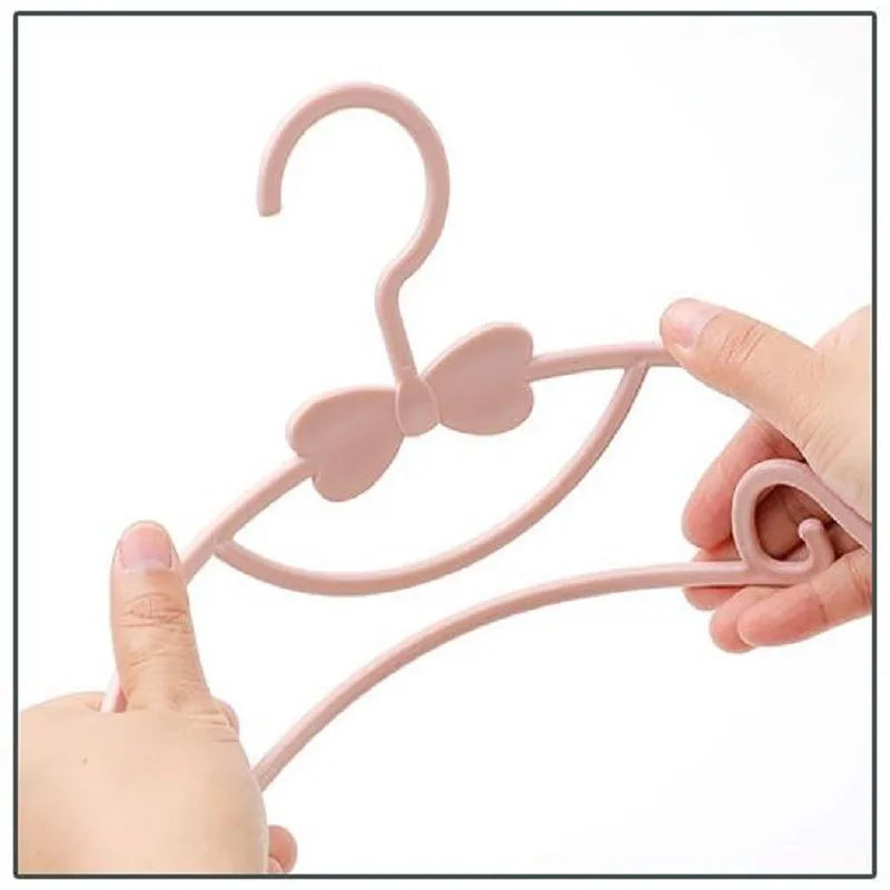 Pink plastic baby clothes hanger with a decorative bow, held by hands.