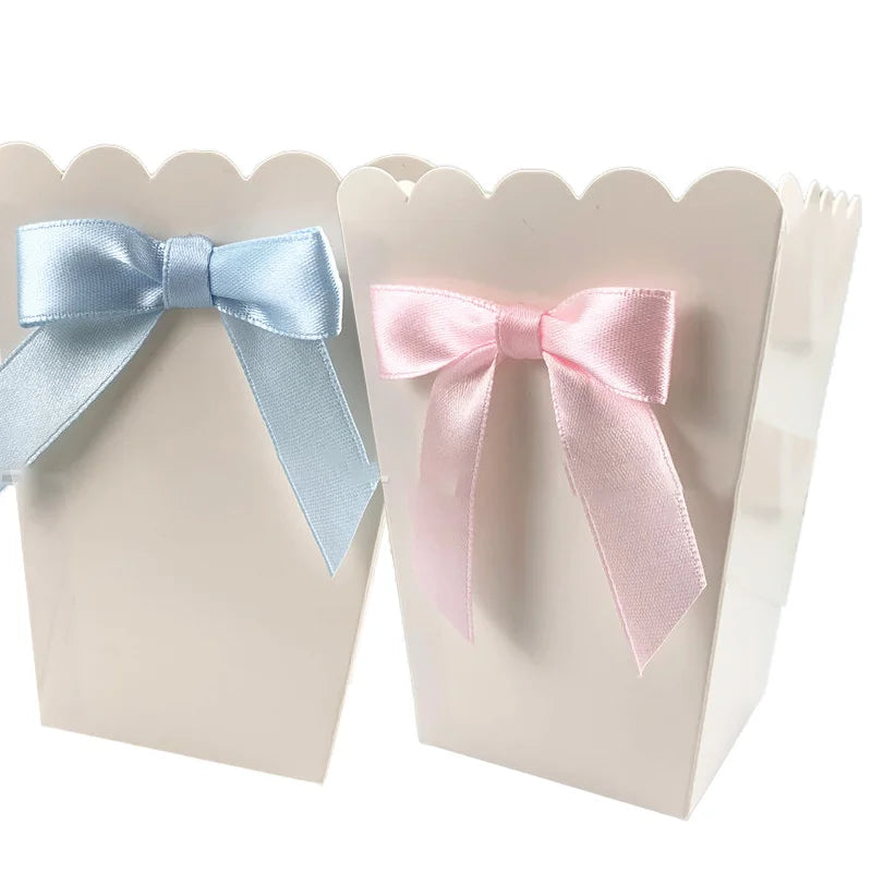 White paper popcorn boxes with scalloped edges, adorned with a blue and a pink satin bow.