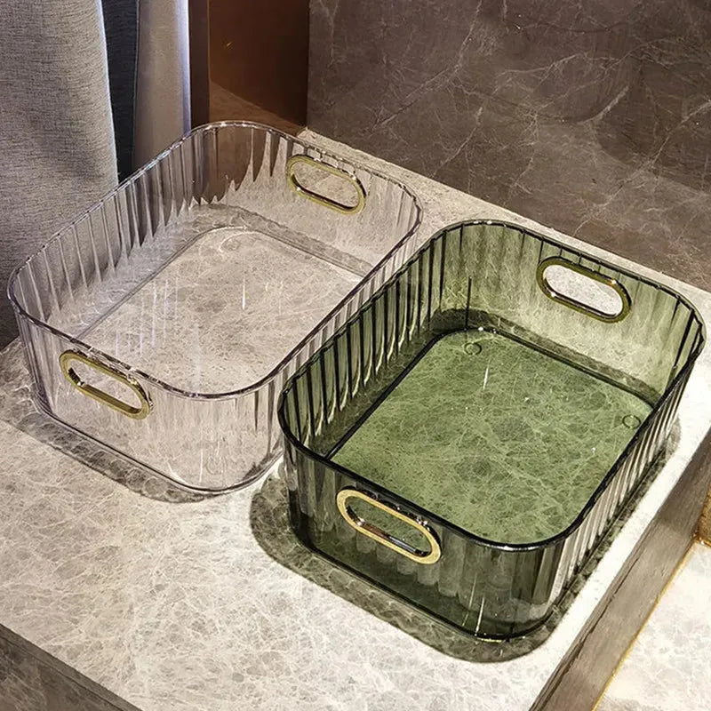 Two rectangular clear PET storage bins with gold handles, one transparent and one green, on a marble surface.