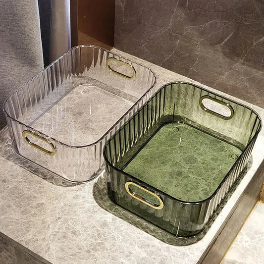 Two rectangular clear PET storage bins with gold handles, one transparent and one green, on a marble surface.