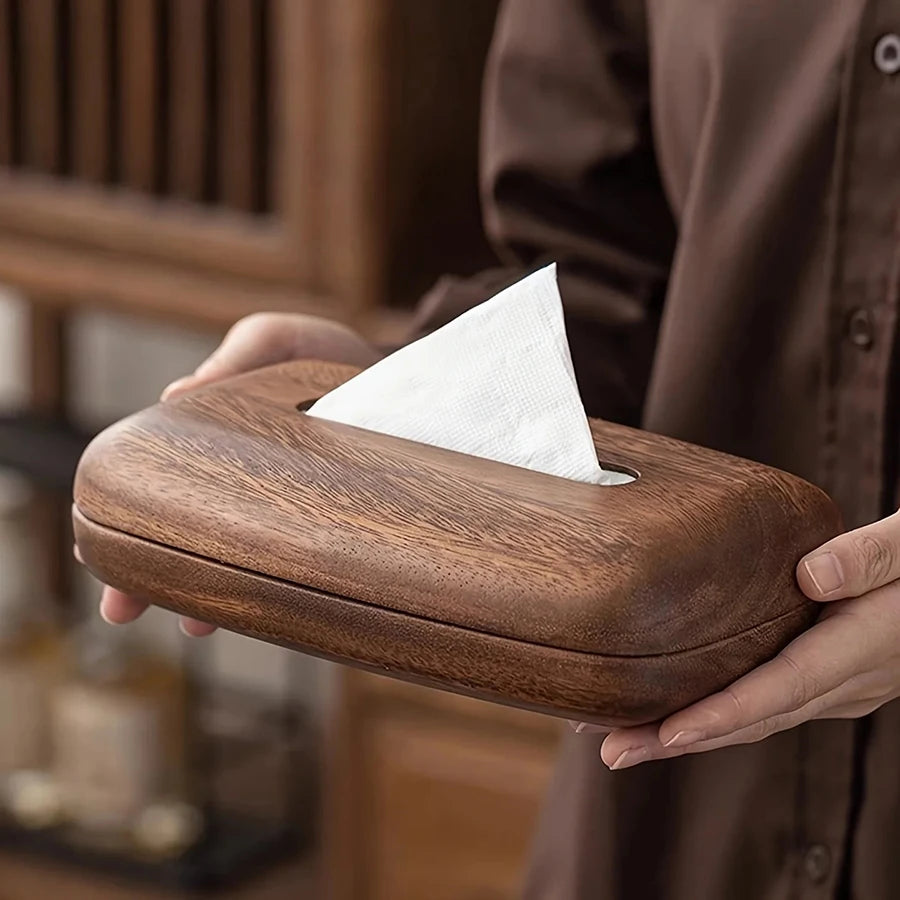 Vintage dark wood tissue box held by hands, featuring a curved, sleek design and a tissue peeking out.