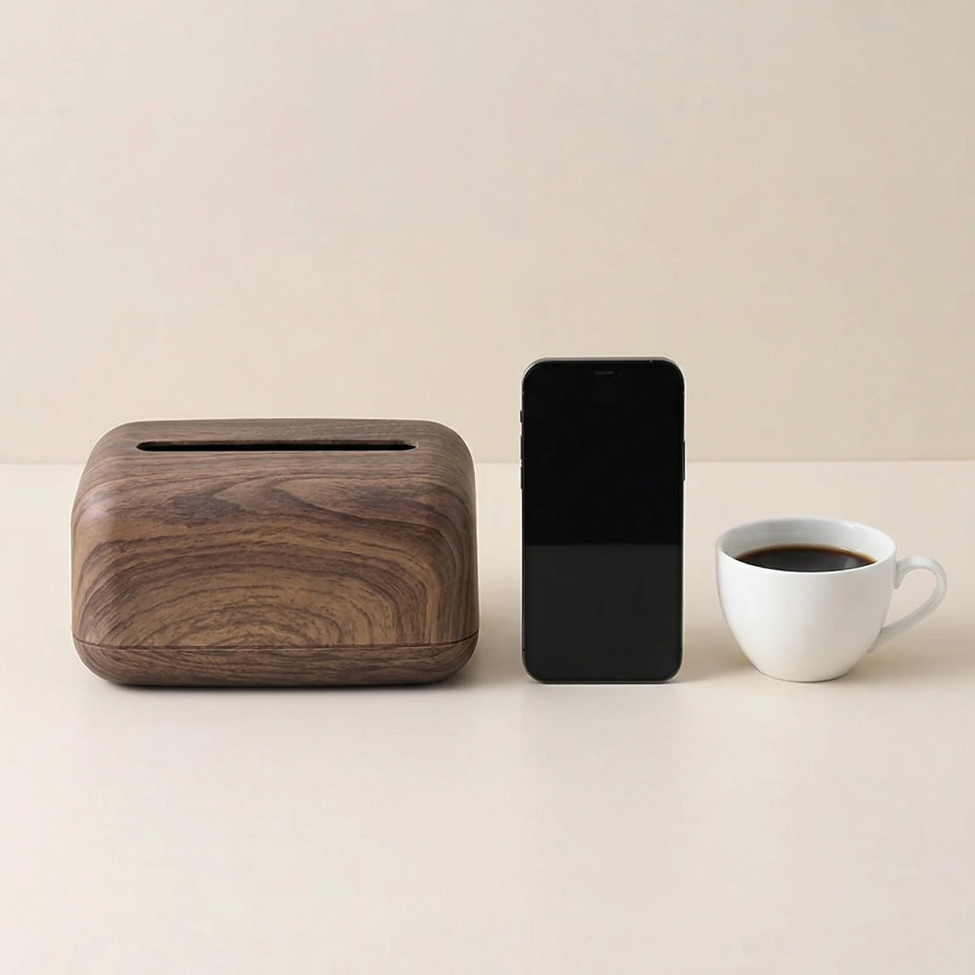 Vintage wood-look tissue box dispenser, next to a smartphone and white coffee cup, on a light background.