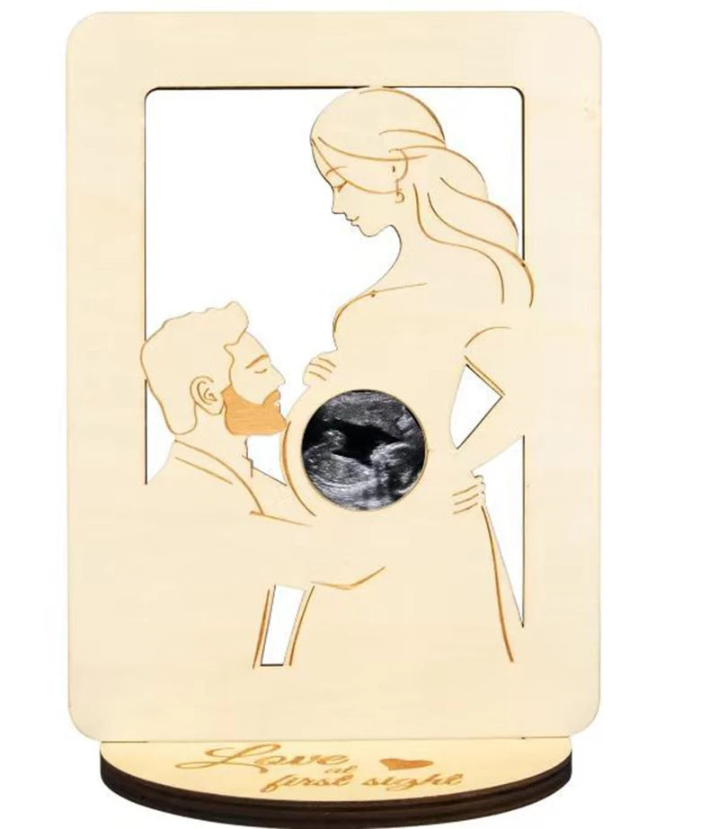 Wooden pregnancy keepsake frame with cutout of a couple, a sonogram in the belly, and "Love at first sight" engraved.