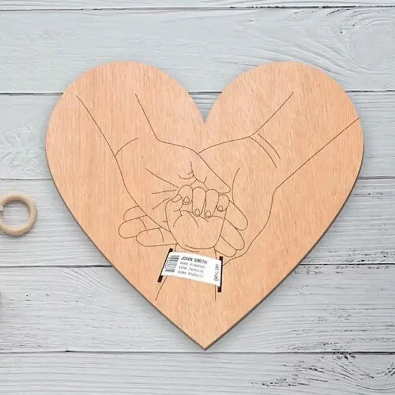 Heart-shaped wooden birth keepsake with engraved parent and baby hands, designed to hold a hospital bracelet.