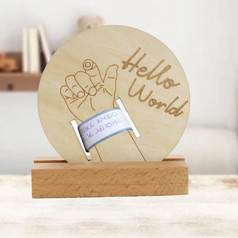 Wooden circular birth keepsake with "Hello World" engraving, baby hand illustration, and slot for hospital bracelet.