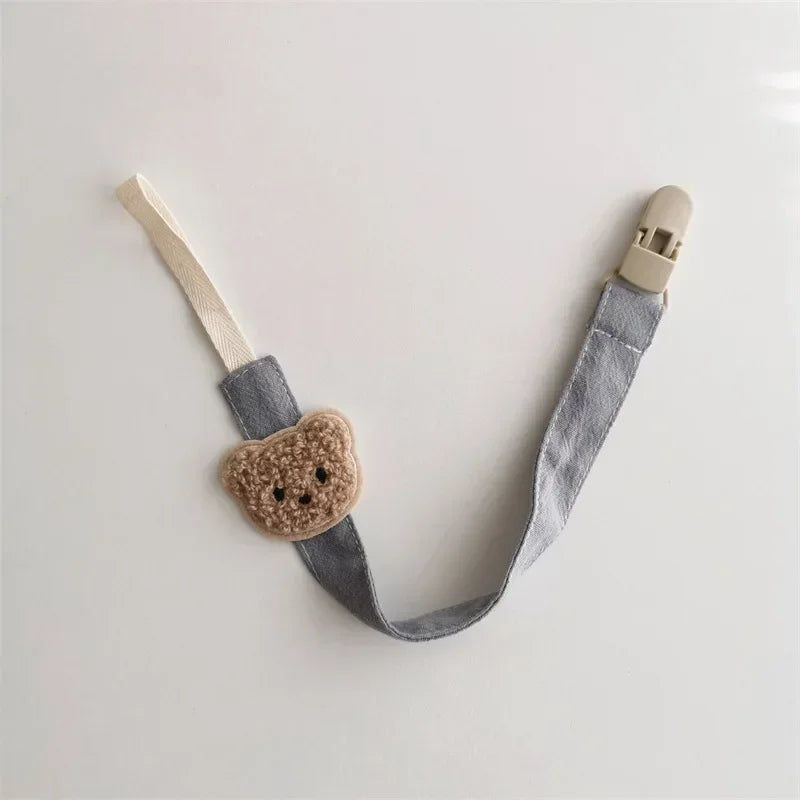 Soft gray cotton pacifier clip with a cute embroidered brown teddy bear and beige plastic clasp.