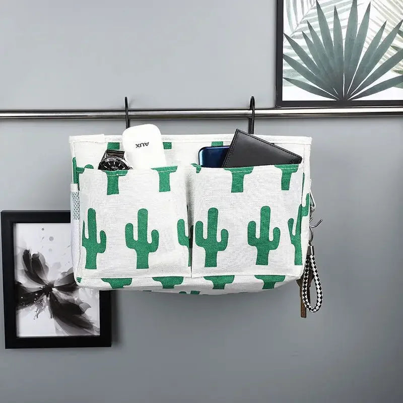 White multi-pocket cotton bed organizer with green cactus print, hanging on a metal rail.
