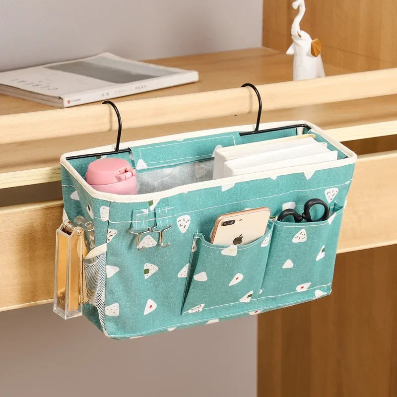 Green multi-compartment cotton bed organizer with white triangle pattern, hanging from a wooden desk.