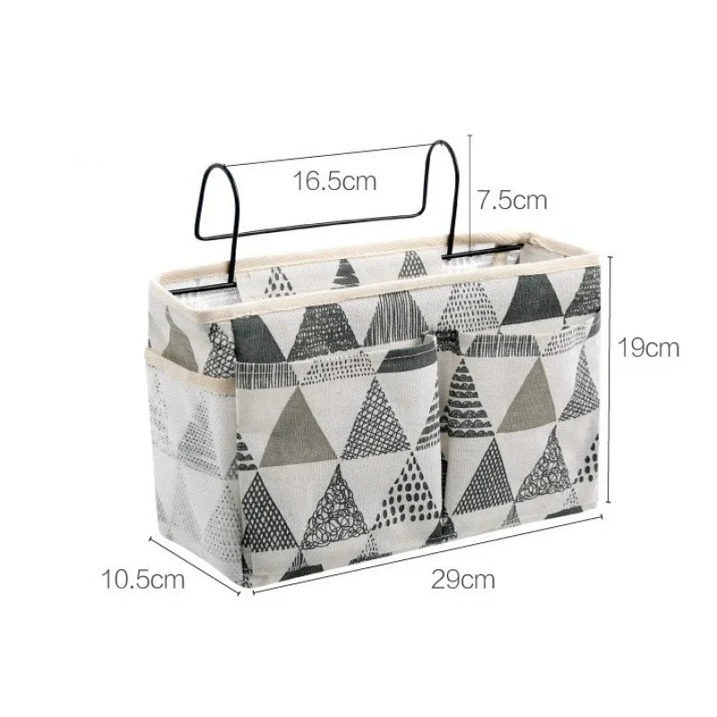 Cotton multi-compartment bedside storage organizer with black and white triangle pattern, hanging on a metal hook.