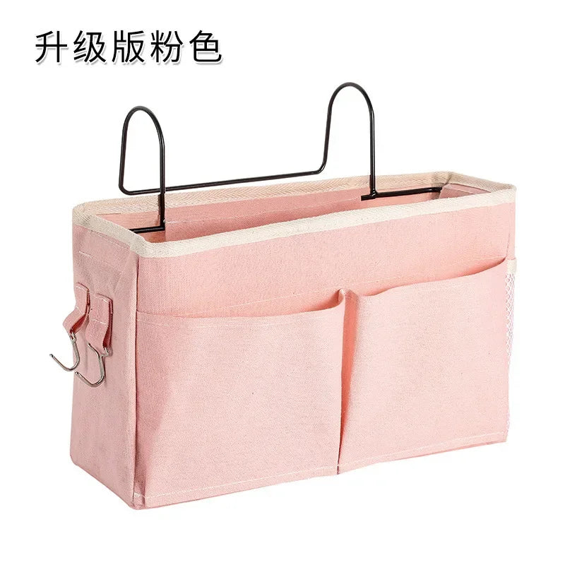 Pink multi-compartment cotton blend bedside caddy with two front pockets and metal hooks for baby essentials.