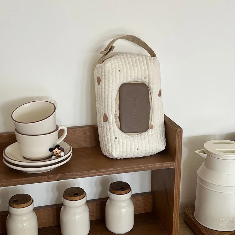 Quilted cream cotton hanging tissue and wipe dispenser with brown heart accents and strap.