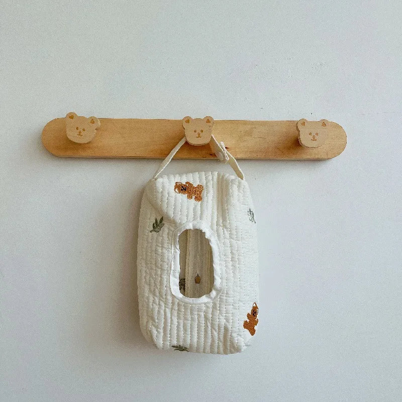 Quilted white cotton tissue and wipe holder with embroidered bears and leaves, hanging from a wooden bear hook.