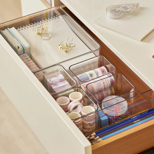 Clear acrylic drawer organizers for desk supplies like notebooks, tape, and pencils.