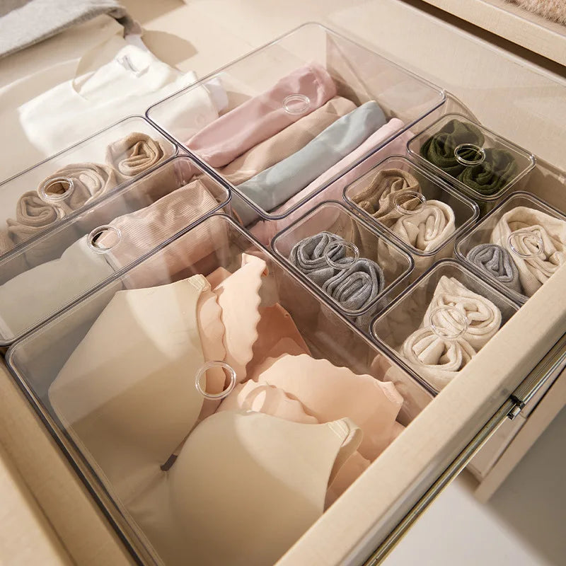 Clear acrylic drawer organizers holding neatly folded bras, socks, and underwear in a light wood drawer.