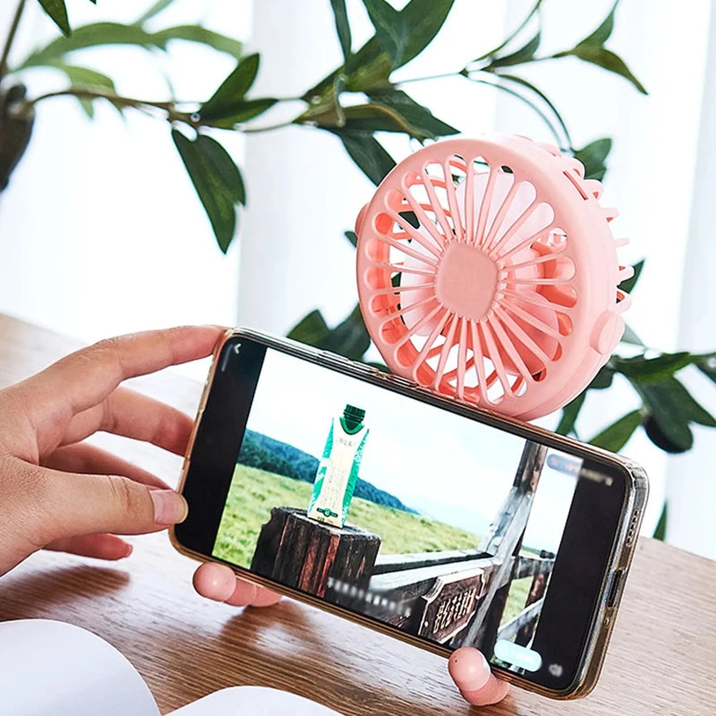 Pink portable USB rechargeable fan with a flexible octopus-style tripod base, holding a smartphone.