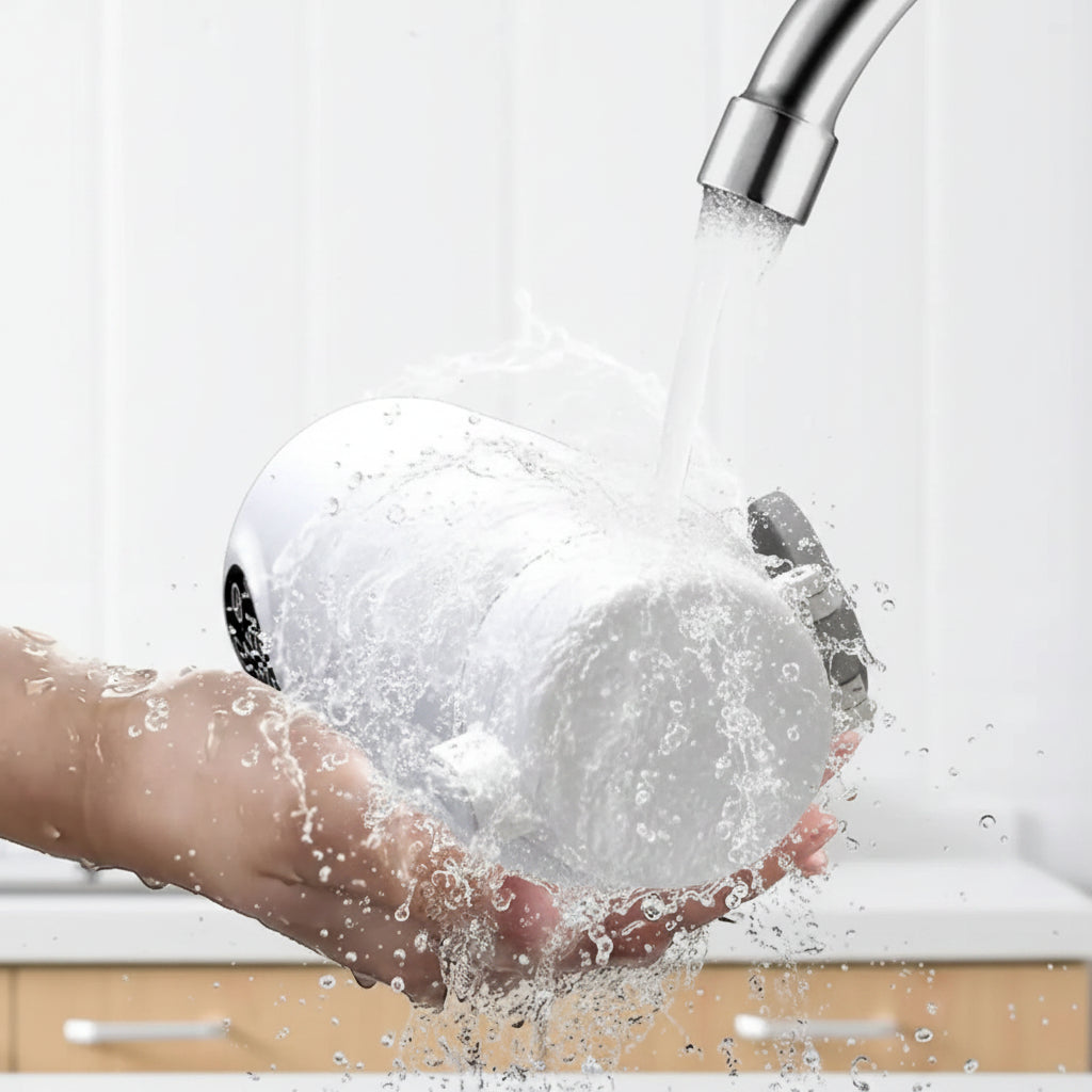 White portable bottle warmer, IPX6 washable, held under running water from a silver faucet.