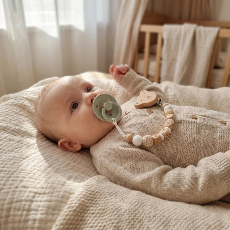 Baby with personalized pacifier clip featuring natural wood and silicone beads, a bear clip, and a sage green pacifier.