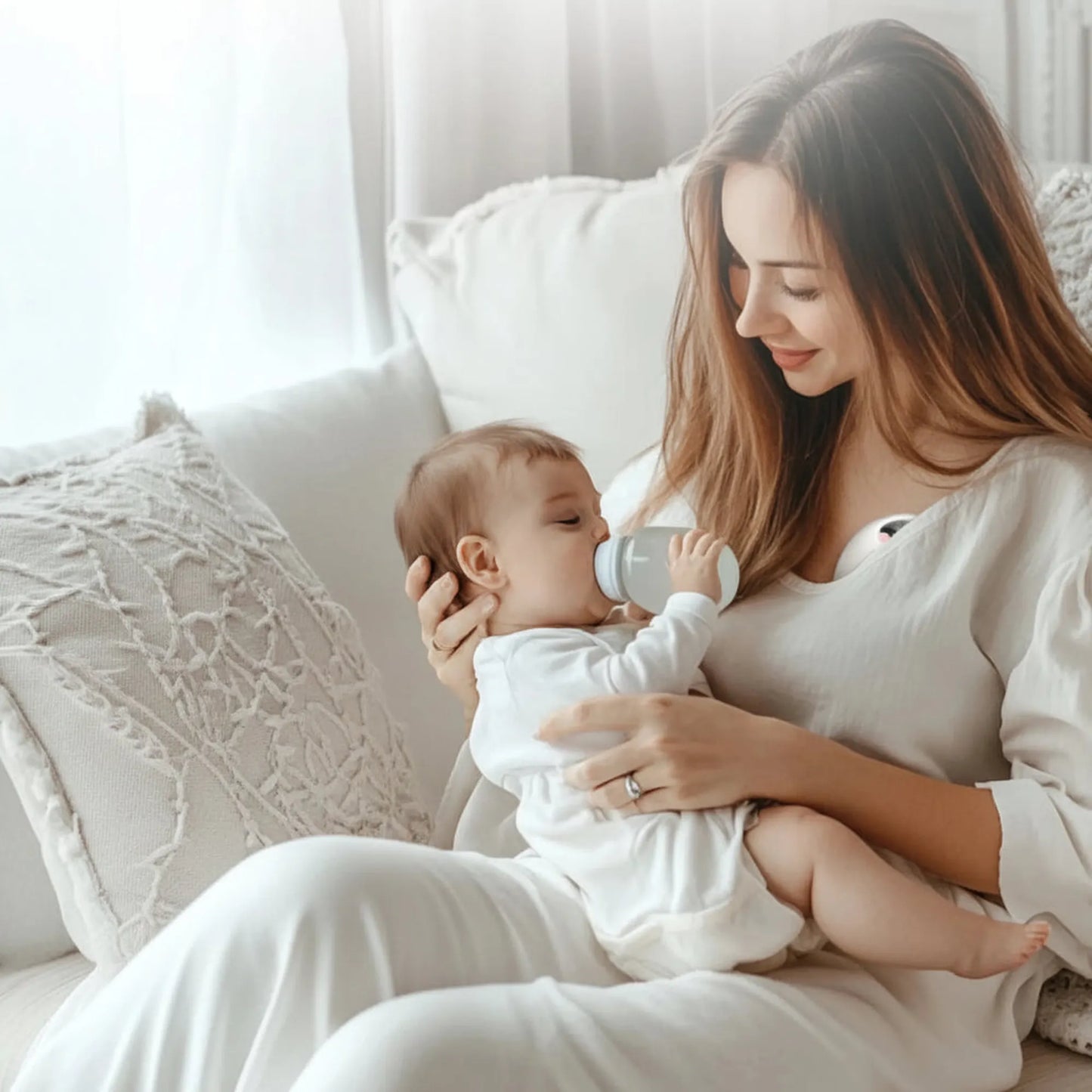 Mother feeding baby a bottle while wearing a discreet, hands-free white electric breast pump.