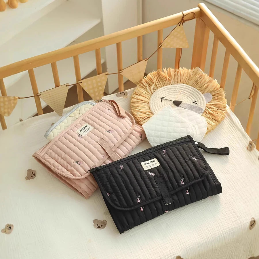 Portable quilted changing pad in pink and black with storage, on a crib with a lion toy.