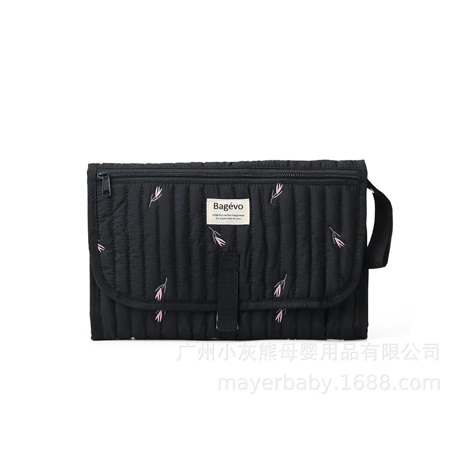 Black quilted portable changing pad with pink floral embroidery and storage pouch.