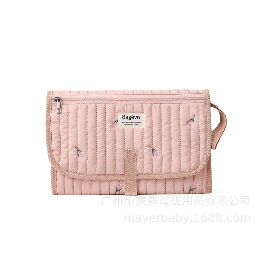 Pink quilted portable baby changing pad with floral embroidery and storage pouch.