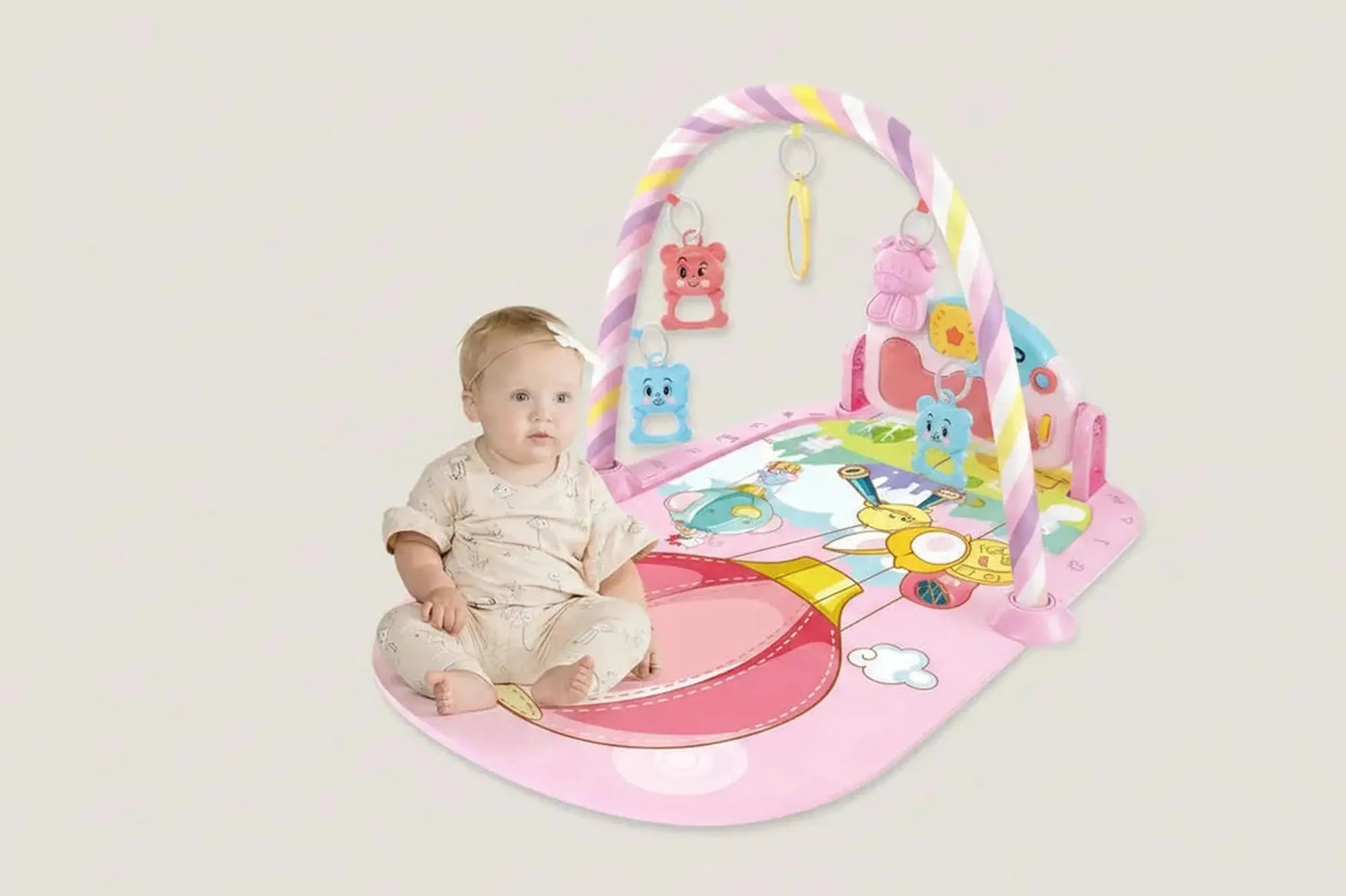Baby on a pink musical play mat with a piano, colorful arch, and hanging animal toys.