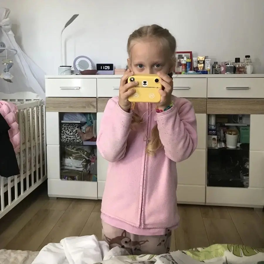 Young girl holding a yellow instant print digital camera for kids, shaped like a cartoon animal.