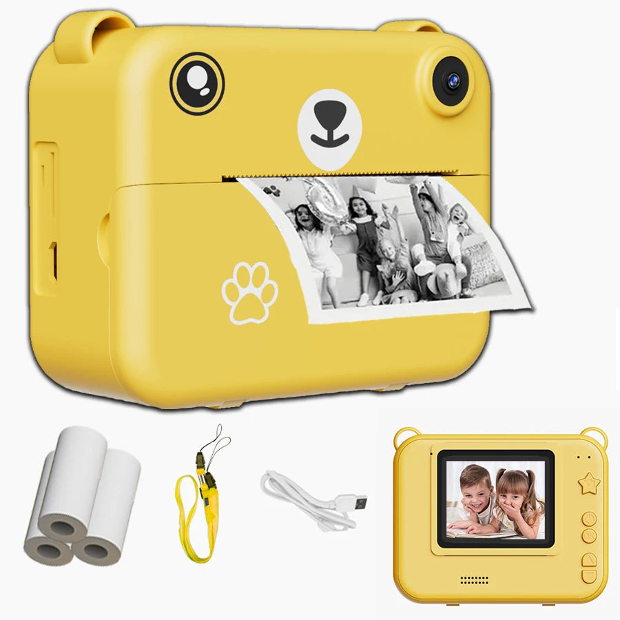 Yellow bear-shaped kids' instant print camera with a black and white photo, strap, charging cable, and paper rolls.