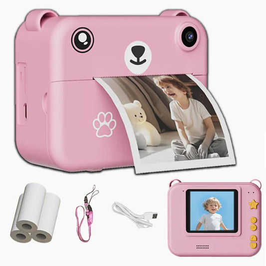 Pink bear-shaped instant print camera for kids, with a printed photo, paper rolls, strap, and charging cable.