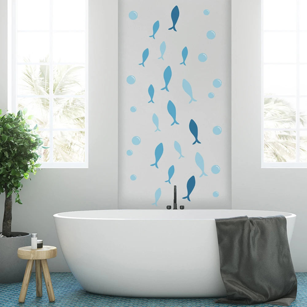 Blue fish and bubble wall decals decorating a white bathroom wall above a modern bathtub.
