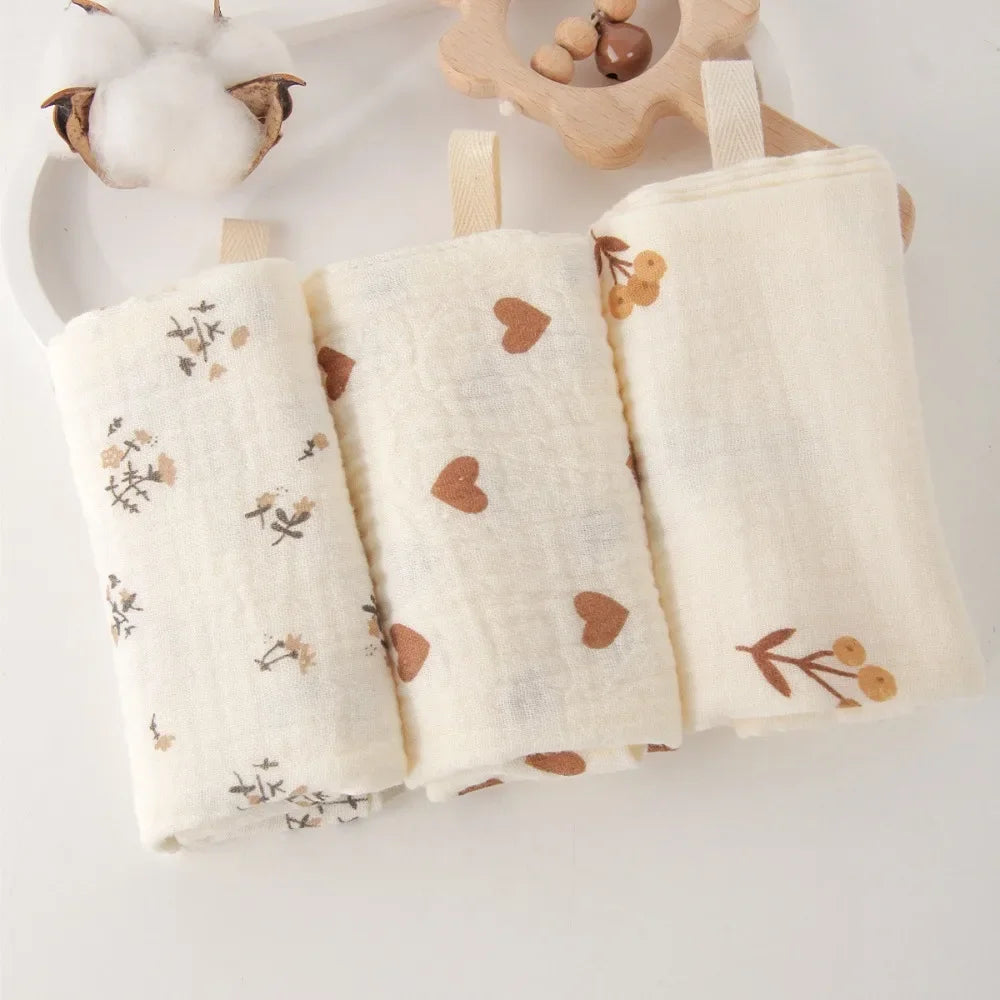 Three soft, natural cotton gauze baby towels with subtle floral and heart patterns.
