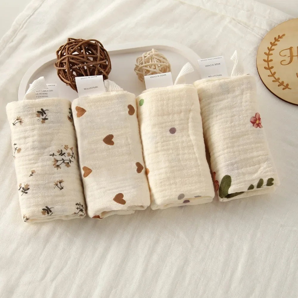 Four rolled white 100% cotton gauze baby towels with various prints: floral, hearts, dots, and a single flower.