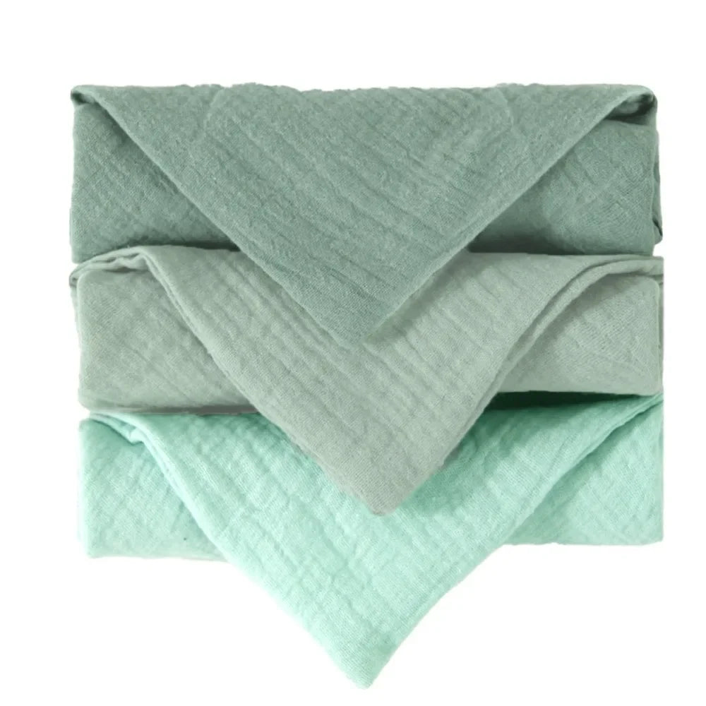 Stack of three soft, folded baby gauze cotton towels in varying shades of light green.