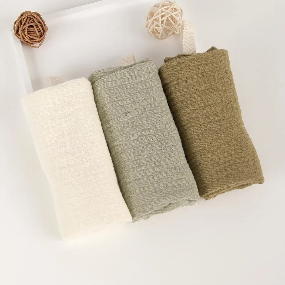 Three rolled 100% cotton gauze baby towels in cream, sage green, and olive green, with hanging loops.