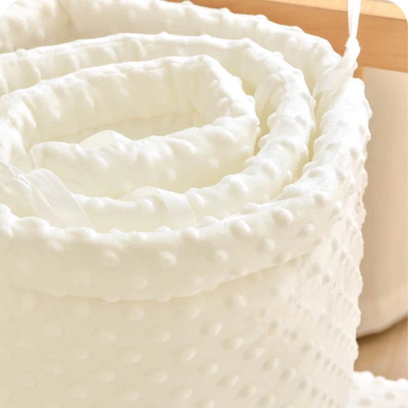 Soft cream polyester crib bumper with textured minky dots and tie straps.