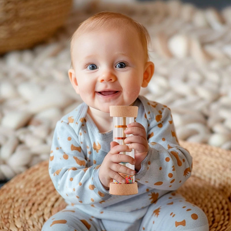 Smiling baby holding a Montessori rainbow rain stick sensory toy with wooden ends and colorful beads.