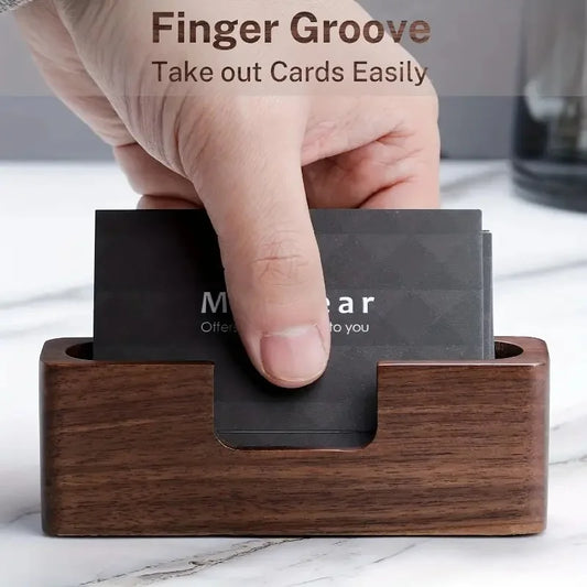 Dark wood business card holder with a finger groove, holding black cards, on a marble surface.
