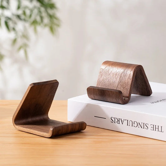 Two minimalist dark walnut wood phone stands, one upright and one angled, on a white book.