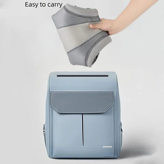 Foldable gray ergonomic baby carrier held above a light blue backpack, demonstrating portability.