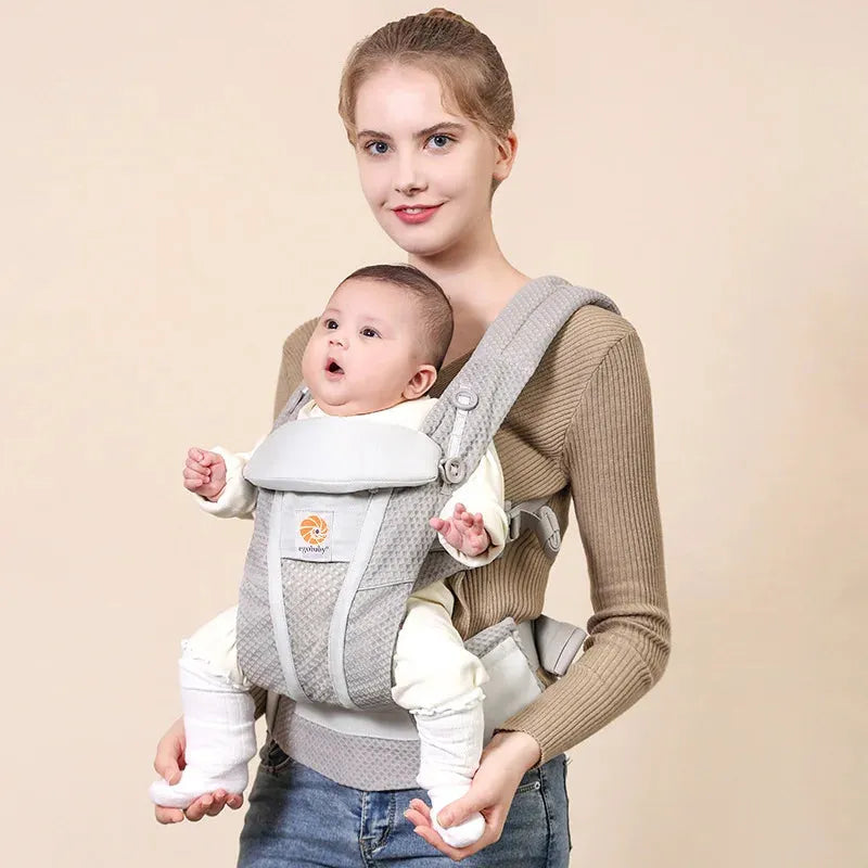 Woman carrying baby in a gray ergonomic Ergobaby carrier with adjustable straps and breathable mesh.