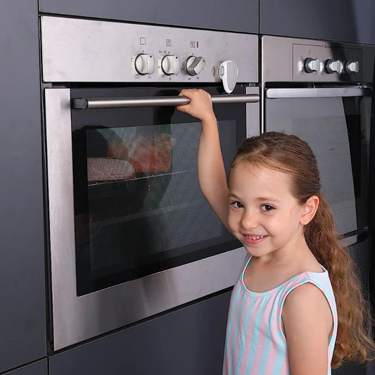 Child-proof gray safety lock on a stainless steel oven, with a smiling girl reaching for the handle.