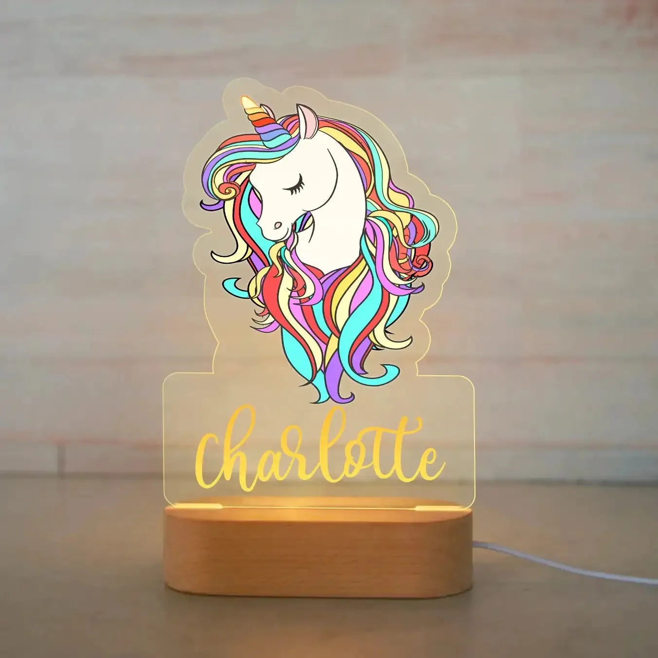 Personalized unicorn night light with colorful mane, "Charlotte" in gold, on a wooden base.