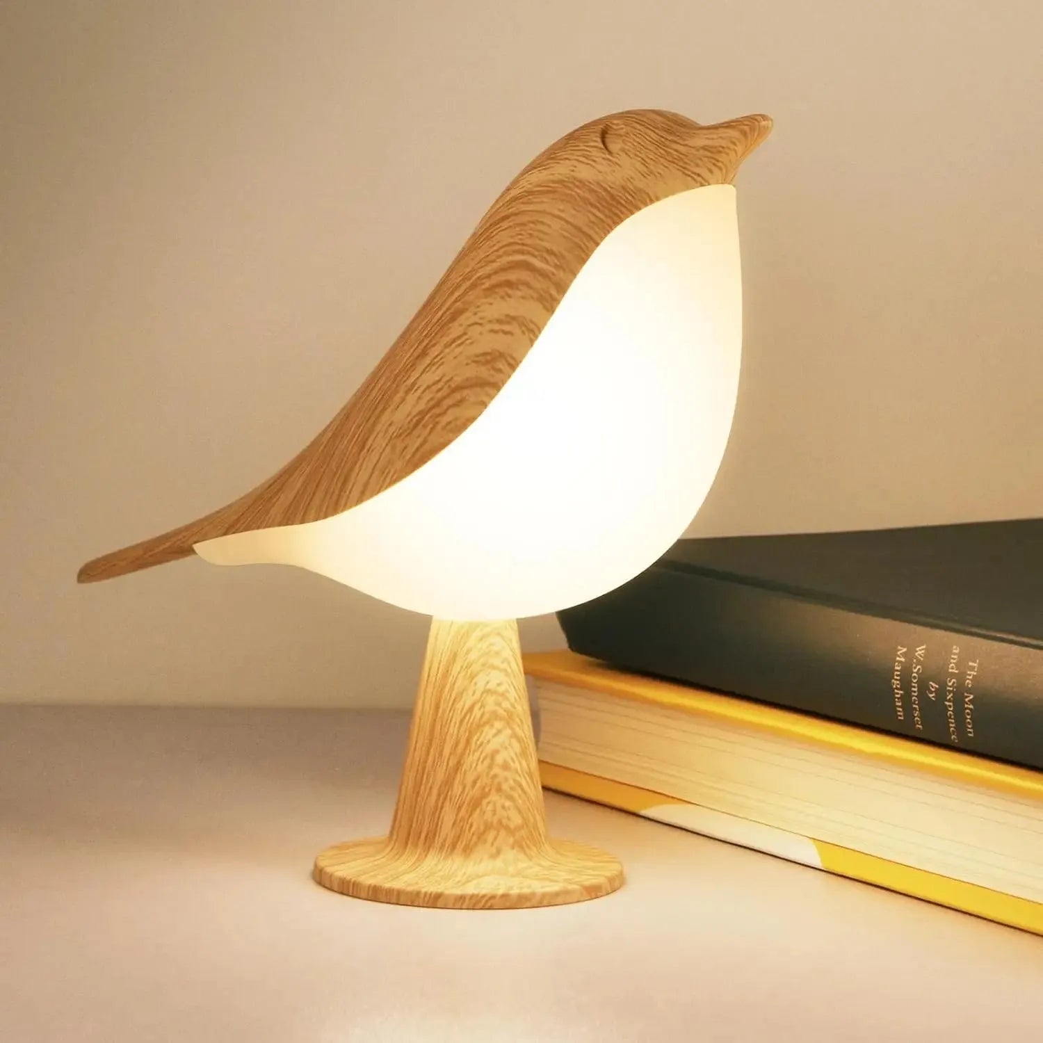 Wooden bird-shaped LED night light with soft glow, on a table next to books.