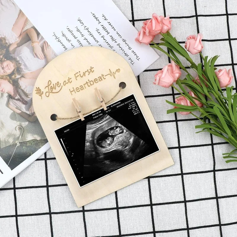 Natural wood ultrasound photo frame with "Love at First Heartbeat" engraving, holding a sonogram with mini clothespins.