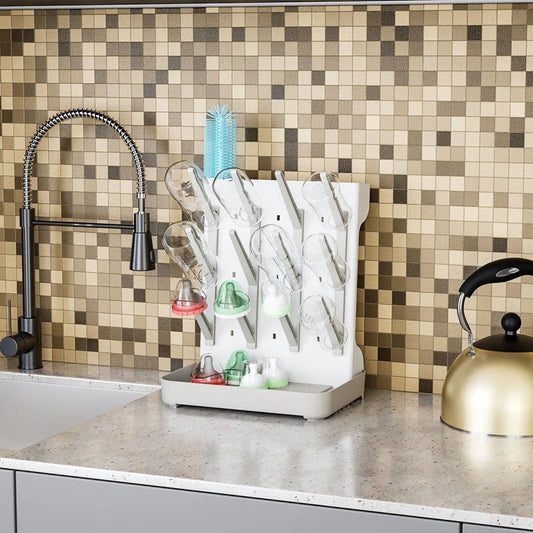 White multi-tier baby bottle drying rack with clear bottles, nipples, and brush on a kitchen counter.